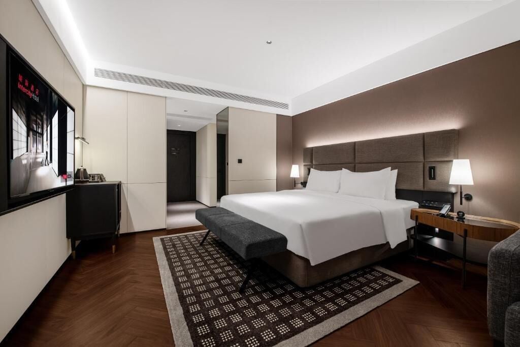 A modern hotel room with a large bed, bedside tables, a desk, and a view of the hallway.