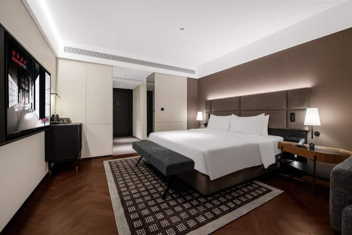 Una habitación de hotel moderna con una cama grande, mesitas de noche, un escritorio y vistas al pasillo.