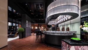 Un'area bar moderna con un bancone curvo, posti a sedere e un grande lampadario.