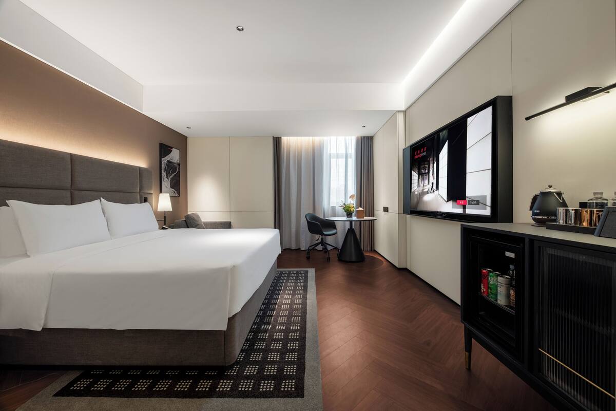 Habitación de hotel con cama, escritorio, silla, televisor y minibar.