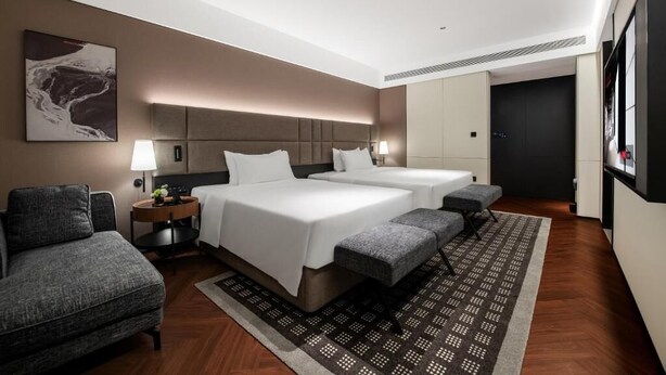 Una camera d'albergo moderna con un letto grande, un letto più piccolo, un divano, una scrivania e una TV.