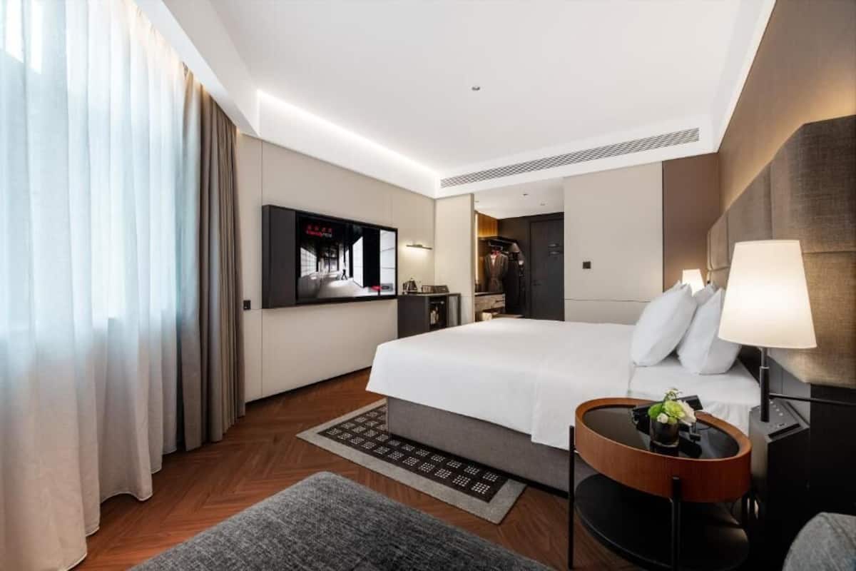 Una habitación de hotel moderna con una cama grande, un televisor de pantalla plana, un escritorio con lámpara y una mesita auxiliar.