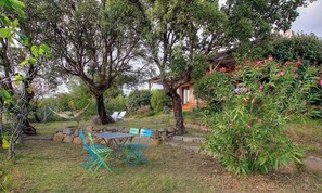 A garden with a table and chairs, a stone wall, and a wooden structure. - Myrtle - MONACIA D'AULLENE (MONACIA D'AULLENE)