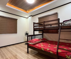 A bunk bed with a red floral bedspread, a wooden ceiling with a recessed light, and a wall-mounted fan.