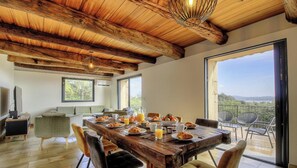 Zona pranzo con tavolo di legno apparecchiato per la colazione, un divano e una televisione sullo sfondo.