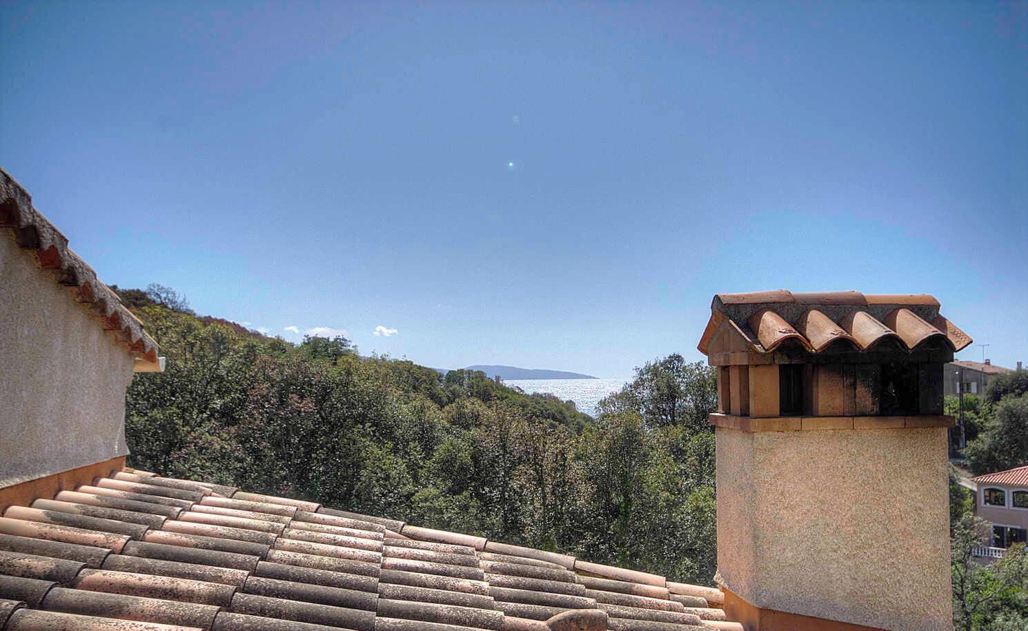 A building with a tiled roof and a chimney, surrounded by greenery and a clear sky.