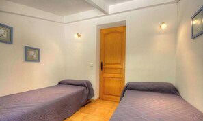 Una habitación con dos camas individuales, una puerta de madera y dos lámparas fijadas a la pared.