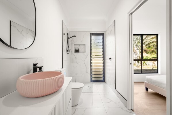 Un baño moderno con suelo de mármol, lavabo rosa, inodoro y ducha.