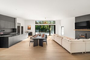 A modern kitchen with a dining area, a large window, and a TV.