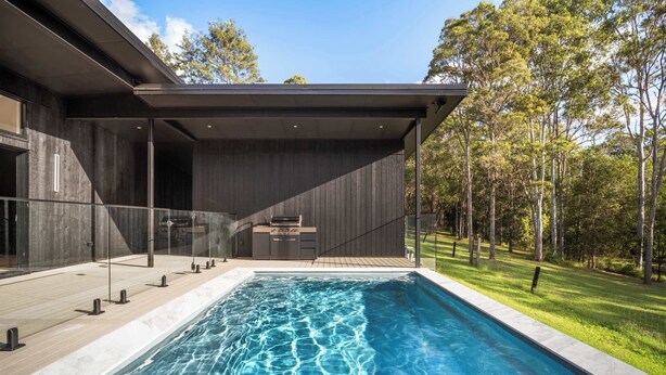 A modern house with a swimming pool, a covered patio, and a view of a forest.
