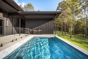 Una casa moderna con piscina, un porche cubierto y vista a un bosque.