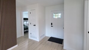 Um corredor com parede de painel de madeira, uma porta branca com janela e um tapete preto na entrada.