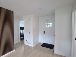 Ein Korridor mit einer Holzwandverkleidung, einer weißen Tür mit Fenster und einer schwarzen Fußmatte am Eingang.