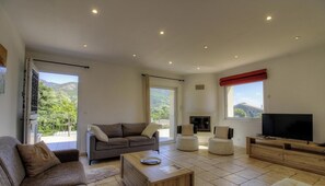 Ein großzügiges Wohnzimmer mit einer Couch, Sesseln, einem Couchtisch, einem Fernseher und einem Kamin.