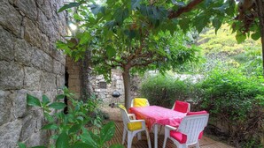 Une terrasse avec une table et des chaises, un mur en pierre et un barbecue.