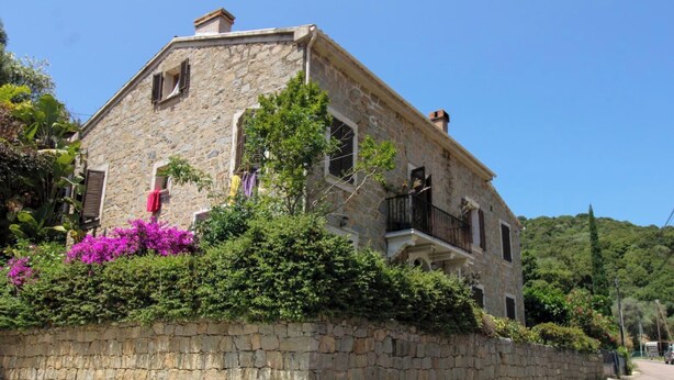 Un bâtiment en pierre doté d’un balcon, entouré d’une végétation luxuriante et de fleurs.