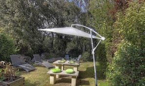 Eine Terrasse im Freien mit Tisch und Stühlen, umgeben von viel Grün.