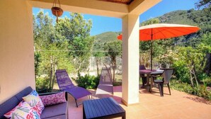Une terrasse couverte, aménagée avec du mobilier d’extérieur, une table et un parasol.