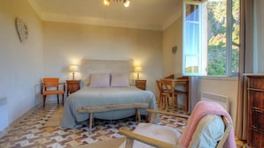 Ein Schlafzimmer mit einem Bett, zwei Stühlen, einem Tisch, einem Heizgerät und einem Fenster mit Blick ins Grüne.