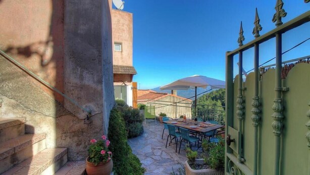 Eine Steintreppe führt zu einer Terrasse mit Tisch und Stühlen, umgeben von Blumentöpfen und Blick auf einen Berg.