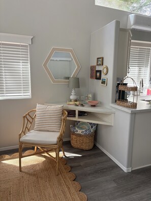 Un coin douillet avec un fauteuil en osier, une petite table avec une lampe, un miroir et un panier.