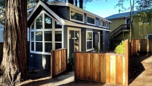 A modern house with a large window, a wooden deck, and a staircase leading to a second floor. - NEW! The Gilded Grove Cottage in Charming Guerneville (Guerneville)