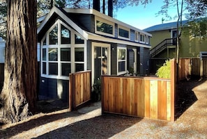 A modern house with a large window, a wooden deck, and a staircase leading to a second floor.