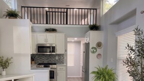 A modern kitchen with white cabinetry, a stainless steel refrigerator, and a dining area with a glass table and chairs. - NEW! The Gilded Grove Cottage in Charming Guerneville (Guerneville)