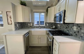 A kitchen with white cabinets, a gas stove, a microwave, and a tiled backsplash.