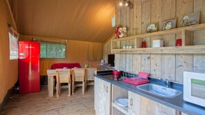 Una cocina compacta con paredes de madera, un refrigerador rojo, una mesa de comedor con sillas y un microondas.