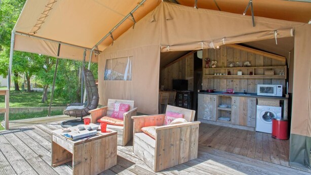 Un espacio exterior con carpa, mobiliario de madera, lavadora y microondas.