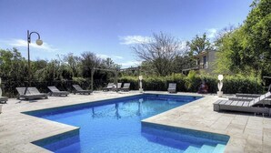Una piscina rectangular con solárium empinado, rodeada de sillas de descanso y una pérgola.