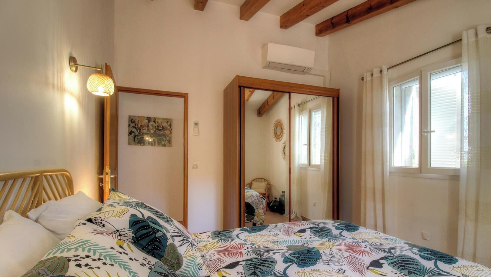 Un dormitorio con cama, espejo, ventana y aire acondicionado.