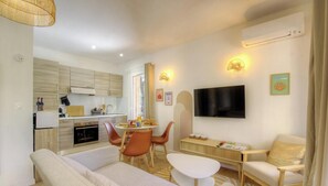 A modern living room with a sofa, dining table, chairs, a TV, and a kitchen in the background. - Pasciale Papanellu - SAINTE LUCIE DE PORTO VECCHIO (SAINTE LUCIE DE PORTO VECCHIO)