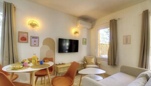A cozy room with a dining table, chairs, a sofa, a TV, and a window with curtains. - Pasciale Papanellu - SAINTE LUCIE DE PORTO VECCHIO (SAINTE LUCIE DE PORTO VECCHIO)