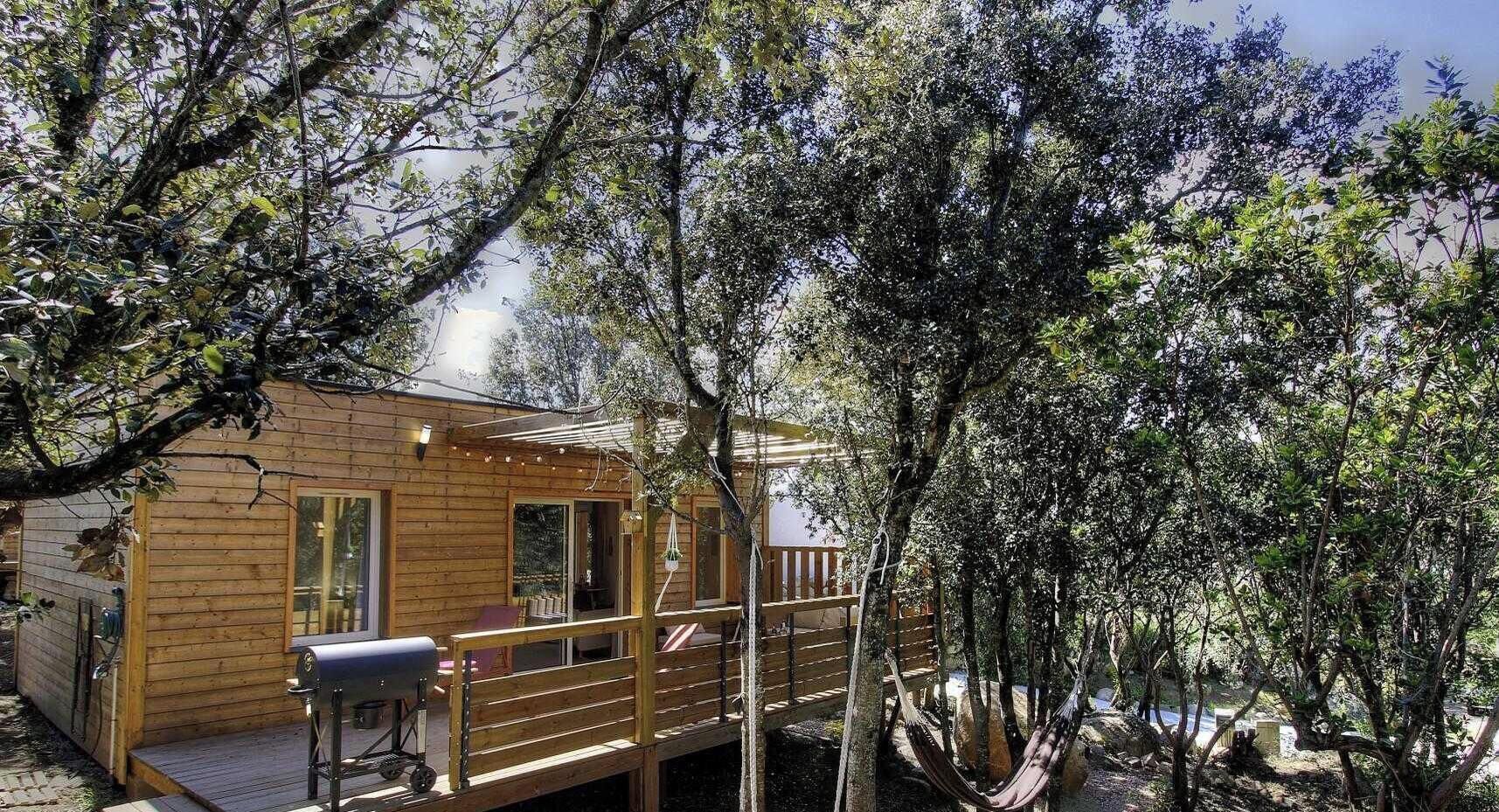Une cabane en bois dotée d’une terrasse, entourée d’arbres.