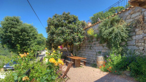 A stone wall with a wooden bench and table, surrounded by greenery and flowers. - Jeannette's welcome (PILA CANALE)