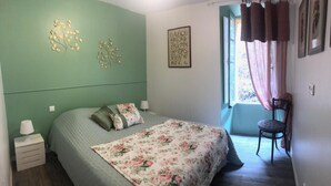 A bedroom with a bed, a chair, a nightstand, a window with curtains, and wall decorations. - Jeannette's welcome (PILA CANALE)