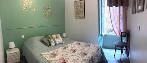Une chambre à coucher comprenant un lit, une chaise, une table de chevet, une fenêtre avec des rideaux et des éléments de décoration murale.