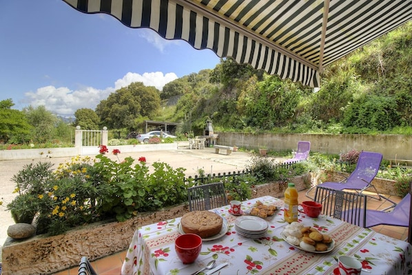 An outdoor dining area with a table set for a meal, surrounded by greenery and a view of a hillside. - Villa Monlabeur 2 - AJACCIO (AJACCIO)