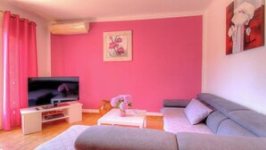 Ein Wohnzimmer mit Flachbildfernseher, einer Couch, einem Couchtisch und einer rosafarbenen Wand.