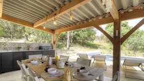Een terras met een houten tafel, stoelen en een keuken op de achtergrond.