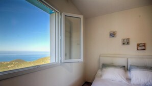Quarto com cama, janela com vista para o mar e um quadro pequeno na parede.