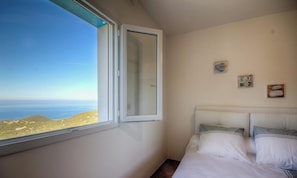 A bedroom with a bed, a window with a view of the sea, and a wall with a small picture. - Clelia - FARINOLE - Gîte (FARINOLE)
