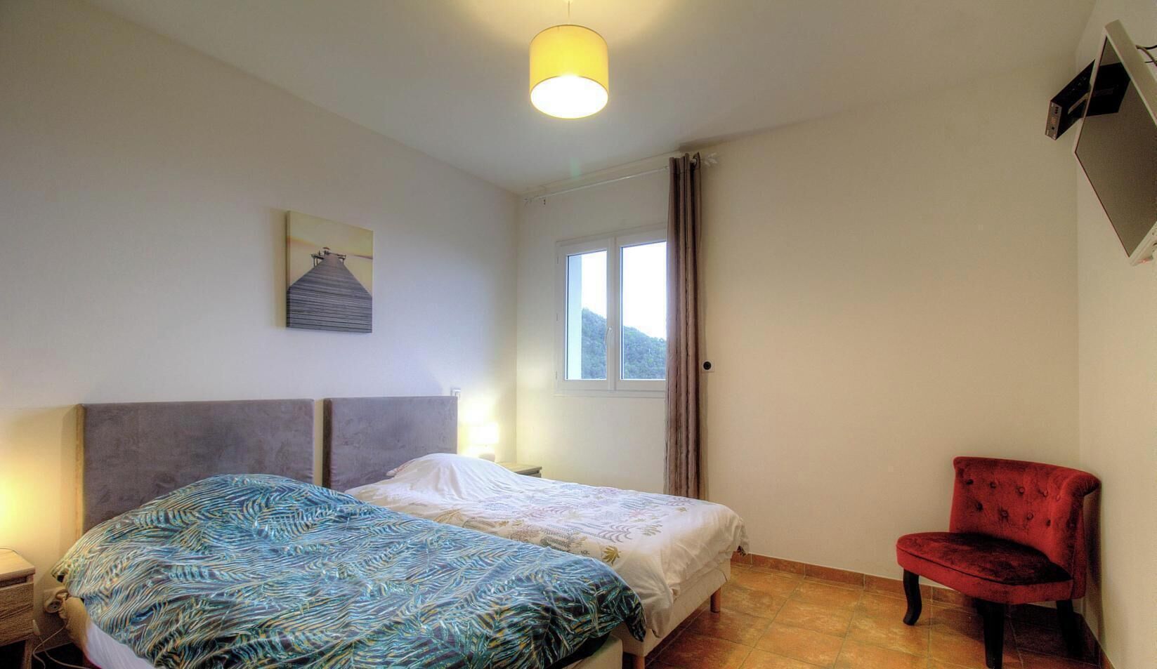 Une chambre avec deux lits, un fauteuil rouge, une fenêtre avec des rideaux et un tableau au mur.