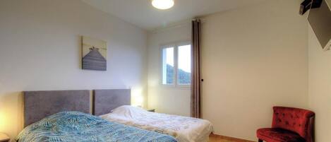 Une chambre avec deux lits, un fauteuil rouge, une fenêtre avec des rideaux et un tableau au mur.