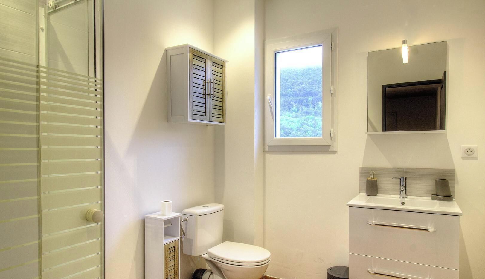 Ein Badezimmer mit Toilette, einem kleinen Fenster, einem Schrank und einem Spiegel.
