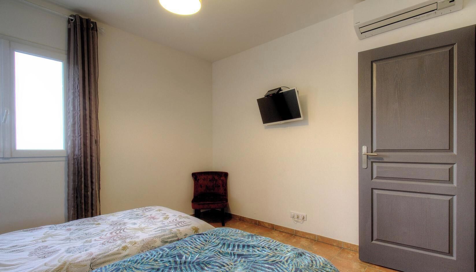 Ein Zimmer mit einem Bett, einem Sessel, einem Fernseher und einer Tür.
