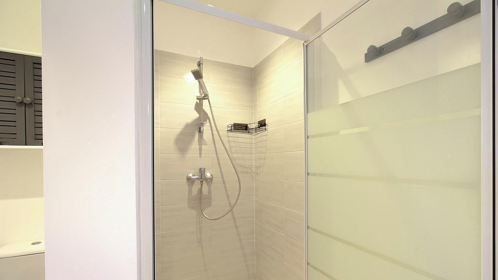 Une douche moderne dotée d’un pommeau de douche à main et d’un robinet mural.