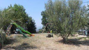 Un'area giochi con scivolo e struttura per arrampicarsi, circondata da erba secca e alberi.